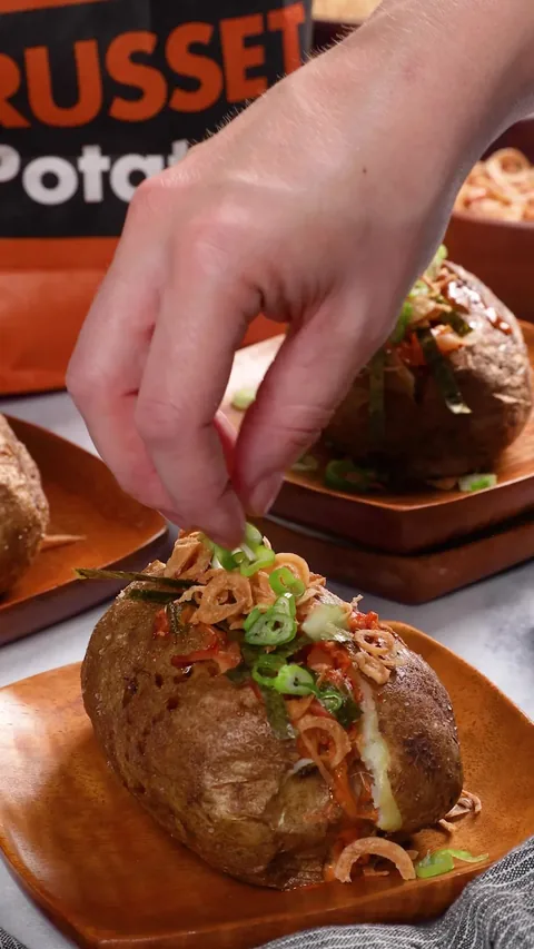 A baked russet split open and topped with spicy mayo, kimchi, nori, green onions and fried shallots.