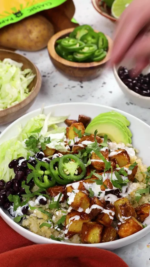 A burrito bowl of chipotle potatoes, black beans, avocado, jalapeño and crema, a bag of Spud & Root Gold Potatoes behind it.